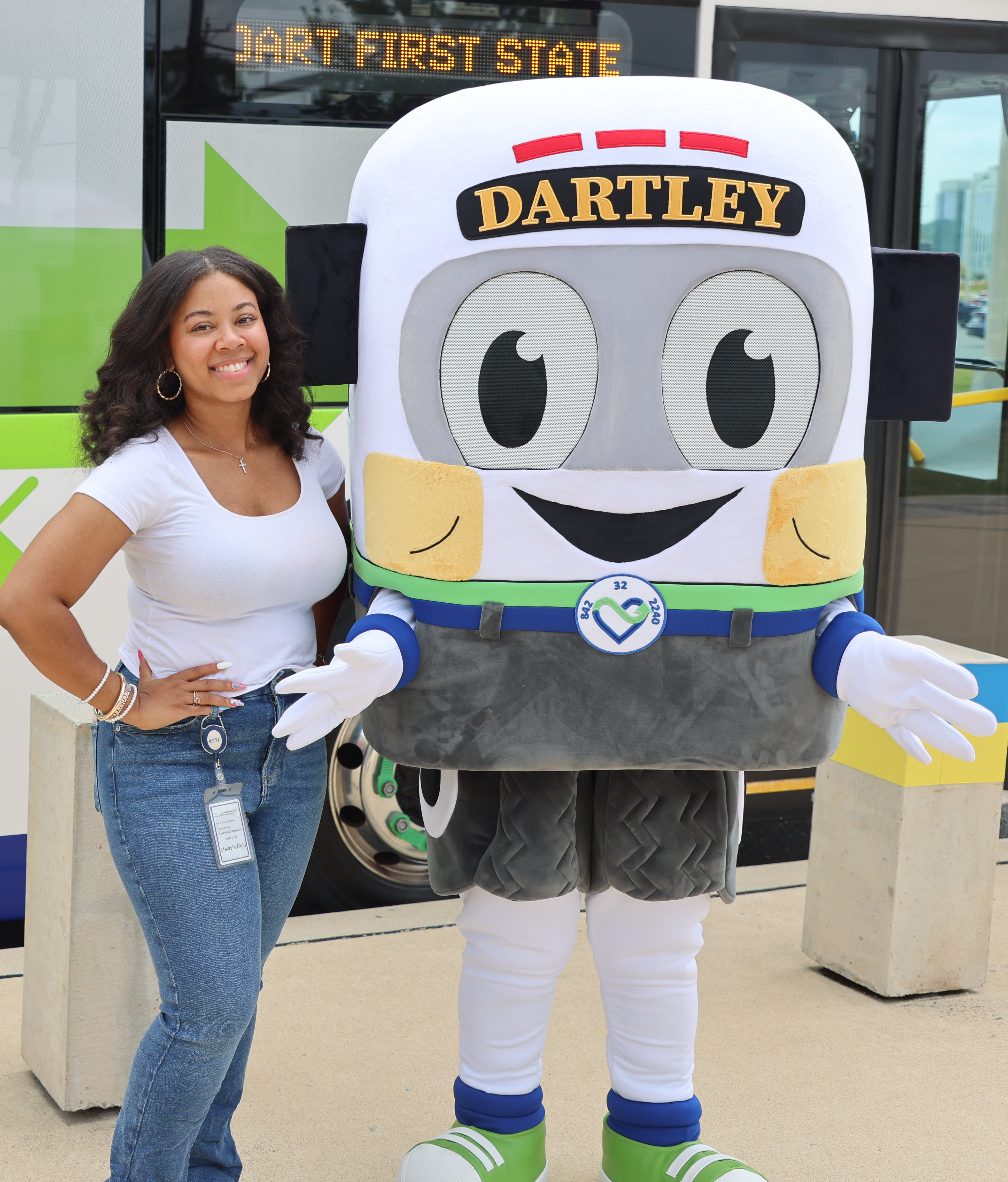 Malasia Reid standing beside the DARTLEY mascot costume in front of a DART bus.